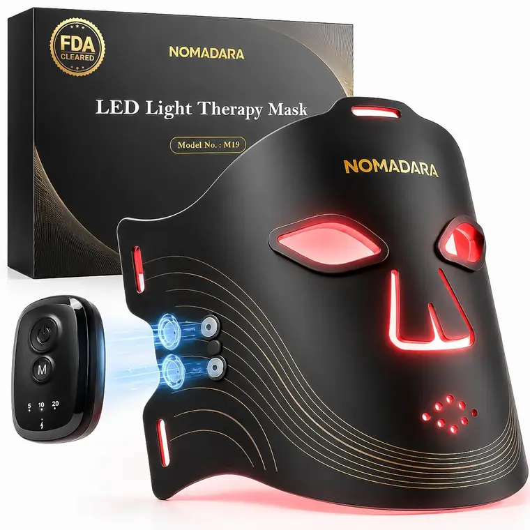 Black NOMADARA LED light therapy mask with glowing red eye, nose, and mouth panels, shown beside its control unit and FDA-cleared product box; sleek, clinical design.